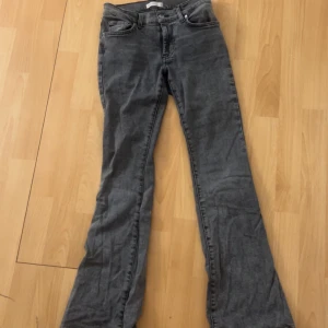 Grå bootcut jeans - Säljer ett par grå bootcut jeans med klassisk femficksdesign och dragkedja. Jeansen har en låg passform och är tillverkade i denim. Perfekta för dig som gillar en tidlös stil med lite utsvängda ben.