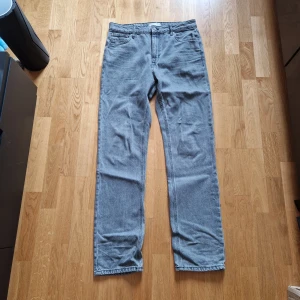 Grå jeansbyxor från ASOS DESIGN - Säljer ett par grå jeansbyxor från ASOS DESIGN i klassisk straight fit. Byxorna har fem fickor, gylf med dragkedja och knapp samt bälteshällor. Perfekta för dig som gillar en enkel och stilren look.