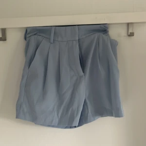 Ljusblå shorts från Amisu - Snygga ljusblå shorts från Amisu med hög midja och bälteshällor. De har en klassisk passform med veck framtill och stängs med dragkedja. Perfekta för varma dagar och lätta att matcha med olika toppar.