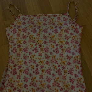 Blommig sommarklänning från Sinsay XS - Supersöt kort klänning från Sinsay i storlek XS. Klänningen är vit med små rosa och gula blommor, har smala axelband och är figurnära. Perfekt för varma dagar och har ett tunt, luftigt material som känns lätt mot huden.