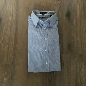 Blå rutig skjorta Tommy Hilfiger - Snygg blå rutig skjorta från Tommy Hilfiger med klassisk krage och bröstficka. Skjortan har vita knappar och lång ärm, perfekt för en clean och stilren look. Materialet är mjukt och andas, vilket gör den skön att bära hela dagen.
