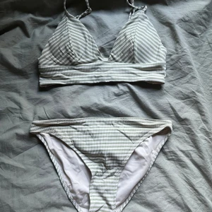 Randig bikini från H&M - Säljer en bikini från H&M i storlek 34. Bikinin är vit med ljusgröna ränder och har en mjuk topp med smala axelband samt matchande trosa. Perfekt för sommaren!