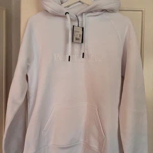 Vit hoodie från Peak Performance - Säljer en klassisk vit hoodie från Peak Performance i storlek L. Tröjan har huva med dragsko, magficka och broderad logga framtill. Aldrig använd, lappen kvar.