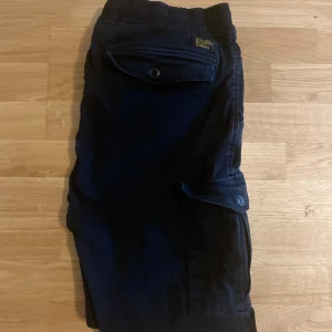 Svarta cargobyxor från Vaillent - Svarta cargobyxor från Vaillent med elastisk midja och dragsko. Byxorna har stora fickor på sidorna och en bakficka med knapp. Perfekta för en avslappnad och trendig stil.