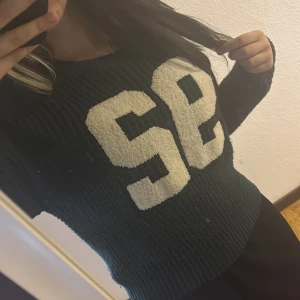 Mörkgrön stickad tröja med SE-tryck - Säljer en mörkgrön stickad tröja med stora vita bokstäver 'SE' framtill. Tröjan har en chunky känsla, rund halsringning och långa ärmar. Perfekt för dig som gillar sportig och avslappnad stil.