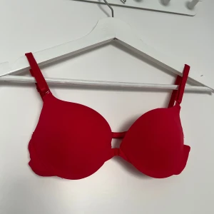 Ny röd push-up bh - Säljer en röd push-up bh i storlek XS med justerbara axelband. Bh:n är tillverkad i mjuk polyesterblandning och har en enkel design utan extra detaljer. Perfekt för dig som vill ha en klassisk och färgstark bh.