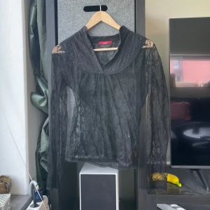 Svart spetsblus från Esisto - Säljer en svart långärmad spetsblus från Esisto. Blusen har transparent spetsmaterial och en snygg krage. Perfekt för dig som vill ha en elegant och trendig topp med unika detaljer.