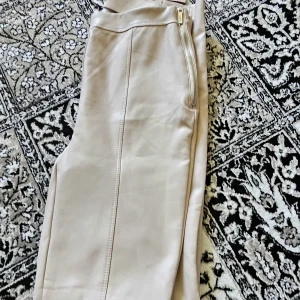 Beiga skinnbyxor med dragkedja - Snygga beiga skinnbyxor med hög midja och dragkedja i sidan. Byxorna har raka ben och en stilren söm längs framsidan. Perfekta för dig som vill ha en trendig och clean look.