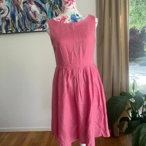 Rosa linneklänning från Maria Westerlind - Säljer en söt rosa klänning i linne från Maria Westerlind. Klänningen har rund halsringning, knappar längs ryggen och en lätt utställd kjol. Perfekt för varma dagar och enkel att styla med accessoarer.