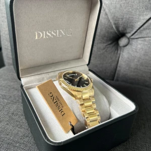 Dissing Day Date Guld 39mm - Helt ny, aldrig använd och stilren Day Date D1746 herrklocka från Dissing med guldfärgad länk och svart urtavla. Kommer i original ask med märkestagg. Köpt från Ditur för 2,195kr. 