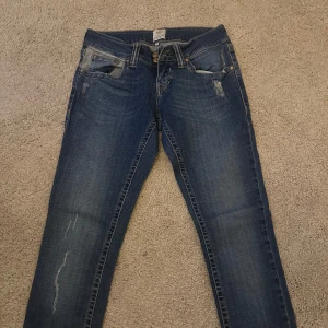 Blå  jeans med små slitningar - Snygga blå jeans från Rive Island med slitna detaljer och klassiska fem fickor. Jeansen har en mörk tvätt med ljusa partier och kontrastsömmar på bakfickorna. Perfekta för en avslappnad och trendig look. Även lågmidjade 💕