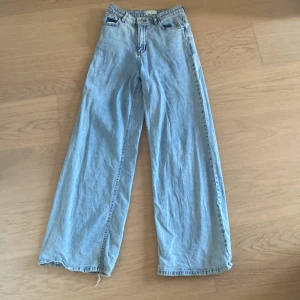 Ljusblå wide leg jeans från Lindex - Säljer ett par ljusblå jeans från Lindex i modellen Viola. Byxorna har hög midja och vida ben för en avslappnad look. Klassisk femficksmodell med dragkedja och knapp framtill. Perfekta till vardags för en trendig stil. Byxorna är snygga och är väldigt sköna. Passar dig som gillar sköna och snygga kläder!