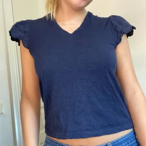 Mörkblå blus med broderade ärmar - Supersöt mörkblå blus med v-ringning och korta puffärmar i broderad bomull. Ärmarna har fina blommiga broderier och vågig kant. Hör av er vid fler frågor 🎀🎀💓