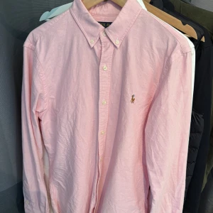 Ralph Lauren skjorta - Säljer en klassisk rosa skjorta från Polo Ralph Lauren i slim fit. Skjortan är nästan helt ny och enbart använd 2-3 gånger o e perfekt för dig som gillar stilrena och tidlösa plagg.