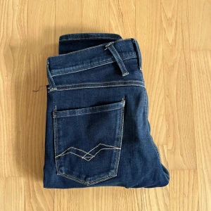 Mörkblå jeans från Replay - Säljer ett par mörkblå jeans från Replay. Jeansen har raka ben och normal passform, perfekt för en stilren vardagslook. Märkeslogga på bakfickan och knappgylf framtill.