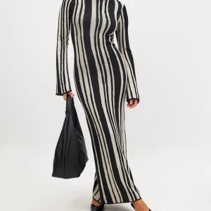 Randig långklänning i svart och beige - Snygg långklänning med svarta och beige/vita ränder. Klänningen har lång vidärm, hög hals och figurnära passform som framhäver siluetten. Perfekt för dig som gillar en stilren och modern look.