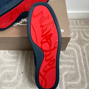 Mörkblå sneakers från Christian Louboutin (pris kan diskuteras) - Snygga mörkblå sneakers från Christian Louboutin i mocka med klassisk röd sula och diskret logga. Skorna har rund tå, platt sula och svarta snören. Insidan är ljusbeige och de levereras med originalkartong och dustbag. Leverans 12-15 dagar