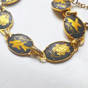 Svart och guldigt armband med motiv - Unikt armband med ovala länkar i svart och guld, dekorerade med detaljerade fågelmotiv. Kedjan har säkerhetslås och hela smycket har en cool vintagekänsla. Perfekt för dig som vill sticka ut med ett smycke som har japansk-inspirerad design.