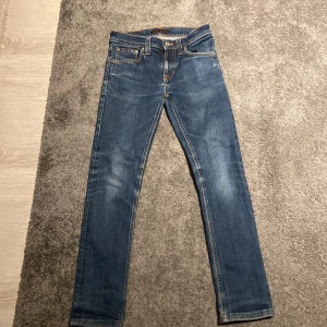 Blå skinny jeans från Nudie Jeans - Säljer ett par klassiska blå slim fit jeans från Nudie jeans. Dom är köpta 2025 och det är väldigt nytt skick