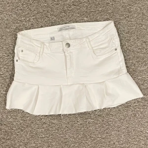 Lågmidjad jeanskjol med volang  - Supersöt vit jeanskjol från Zara med volangkant nertill. Klassisk femficksmodell med knapp och dragkedja framtill.  
