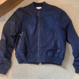 Mörkblå bomberjacka från Stella McCartney Kids - Snygg mörkblå bomberjacka från Stella McCartney Kids med broderade palmblad på framsidan. Storlek 14 år 