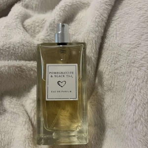 Pomegranate & Black Tea Eau de Parfum - En elegant parfym med doft av granatäpple och svart te. Flaskan är rektangulär i genomskinligt glas med en enkel vit etikett och silverfärgad spraykork. Perfekt för dig som gillar fruktiga och lite kryddiga dofter.