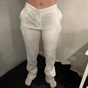 Vita linnebyxor med normal passform - Säljer ett par vita linnebyxor med normal passform och hög midja. Byxorna har raka ben och klassisk design utan synliga detaljer. Perfekta för varmare dagar och ger en fräsch look.