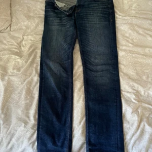 Mörkblå jeans från Jack & Jones Tapered Mike - Snygga mörkblå jeans från Jack & Jones, modell Tapered Mike. Jeansen har klassisk femficksdesign, knappar i gylfen och en något avsmalnande passform. Perfekta för dig som gillar en stilren och tidlös look.
