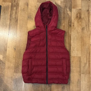 Röd dunväst med huva från Zara - Säljer en röd dunväst från Zara med huva och dragkedja framtill. Pris går att diskutera. Västen har två fickor på sidorna och är perfekt för lager-på-lager under kyligare dagar. Enkel och stilren design. Nästan aldrig använd och i väldigt bra skick. Passar även Liten S p