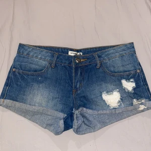 Lågmidjade blå jeansshorts - Säljer dessa blå lågmidjade jeansshortsen med slitningar fram. Storlek s med midjemått 39.  Perfekta för inför sommaren! 🩷