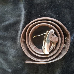 Brunt mockabälte med silverfärgat spänne - Säljer ett brunt bälte i äkta mocka med ett stilrent silverfärgat spänne. Bältet är 100 cm långt och justerbart. Passar perfekt till jeans eller chinos för en snygg och avslappnad look.
