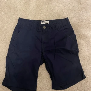 Mörkblå shorts från 157 - Mörkblå shorts från 157 med klassisk passform. De har knapp och dragkedja framtill samt sidofickor. Perfekta för varma dagar och enkla att matcha med olika toppar.