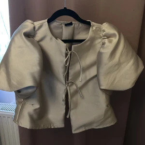 blus - Säljer en beige bolerotopp med korta puffärmar och knytning framtill. Den är som ny använd vid ett tillfälle.