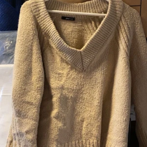 Beige stickad tröja med v-ringning från Gina Tricot - Mysig beige stickad tröja från Gina Tricot med djup v-ringning och bred ribbad kant vid halsen. Perfekt för lager-på-lager och passar till många olika outfits. storlek xs men rätt oversized.