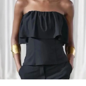 Svart axelbandslös volangtopp - Snygg svart axelbandslös topp med volangdetalj upptill. 