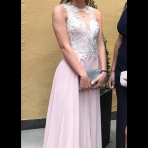 Ljusrosa långklänning med spets och pärlor - Säljer en elegant ljusrosa långklänning med detaljerad spets och pärlor upptill. Klänningen har ärmlös design, hög halsringning och en flytande kjol i mjukt tyg. Perfekt för bal eller festliga tillfällen. Dragkedja i ryggen och vackra broderier framtill. Bara använd 1 gång! Jag är 169 lång och den passar perfekt i längd när jag hade klackar på 7cm! Nypris 3000kr