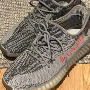 Yeezy Boost 350 V2 Zebra och Black/Red - Två par Adidas Yeezy Boost 350 V2 sneakers, ett par i grått med zebramönster och röd text, och ett par i svart med diskret röd text. Båda har stickad ovandel, snörning och platt sula. Inte min stil längre. 