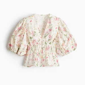 Blommig blus med puffärmar - Superfin blommig blus med v-ringning och puffiga trekvartsärmar. Blusen har smock i midjan och volang nedtill, perfekt för en somrig look. Ljus botten med rosa och gröna blommor. Helt ny med lapp! Passar allt från S till L