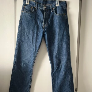 Levi's 501 blå jeansbyxor - Klassiska blå Levi's 501 jeans med raka ben och fem fickor. Byxorna har knappgylf och är tillverkade i slitstarkt denim. Perfekta för en tidlös och avslappnad stil. Levi's Premium-märke och Water<Less-teknologi.