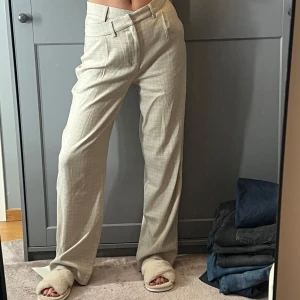Beige rutiga kostymbyxor från Adoore - Snygga beige kostymbyxor från Adoore med diskret rutigt mönster. Byxorna har hög midja med en asymmetrisk touch och raka ben. Oanvända med prislapp kvar! 