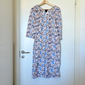Blommig klänning från Lindex - Säljer en ljusrosa klänning från Lindex med blommigt mönster i blått och brunt. Klänningen har trekvartsärm, rund halsringning och en lös passform. Perfekt för vår och sommar! Storlek L. Mycket fint skick, jag hittar inga synliga anmärkningar eller defekter. 