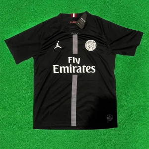 Svart PSG fotbollströja med Fly Emirates - Säljer en svart PSG fotbollströja med Fly Emirates-tryck och Jordan-logga. Tröjan har korta ärmar, rund hals och en grå vertikal rand på framsidan. Perfekt för dig som älskar fotboll och vill visa ditt stöd för Paris Saint-Germain.