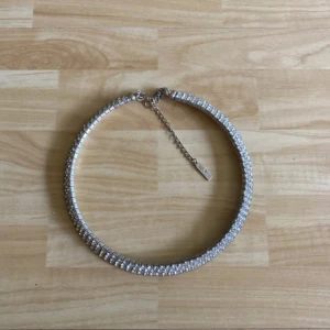 Glittrigt halsband med strass - Säljer ett snyggt halsband i silverfärg med tre rader glittrande strass. Halsbandet har justerbar kedja och ger en lyxig känsla till din outfit. Perfekt för dig som vill sticka ut lite extra.