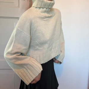 Beige croppad stickad polotröja - Säljer en beige croppad stickad polotröja med breda ribbade muddar och hög polokrage. Tröjan har lång ärm och en oversized passform. Perfekt till kjol eller jeans! Storlek L men skulle säga att den är mindre i storleken. 