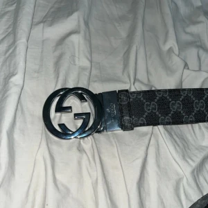 Svart bälte - Säljer ett svart bälte med silverfärgat spänne. Bältet har klassiskt mönster och insida i ljust skinn. Perfekt accessoar för att lyfta din outfit.