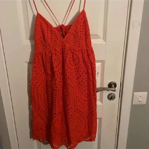 Röd klänning med broderade hål och smala axelband - Superfin röd klänning med broderade hål och smala axelband som korsas i ryggen. Klänningen har v-ringning och är ärmlös, perfekt för varma dagar. Säljs i storlek S. Snygg och luftig modell med fina detaljer.