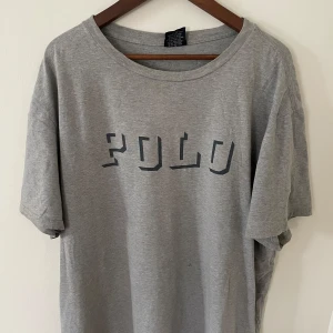 Grå t-shirt från Polo Ralph Lauren - Snygg grå t-shirt från Polo Ralph Lauren med tryckt 'POLO' på bröstet. Klassisk rund halsringning och avslappnad passform. Inga tecken på användning! Storkök XL passar även L