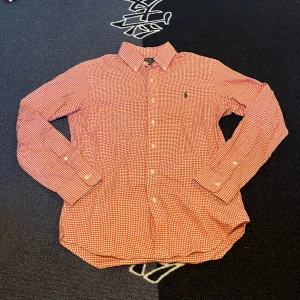 Rutig röd skjorta från Polo Ralph Lauren - Säljer en röd och vit rutig skjorta från Polo Ralph Lauren i slim fit. Skjortan har långa ärmar och klassisk krage. Broderad logga på bröstet. Perfekt för dig som gillar stilrena och klassiska plagg.