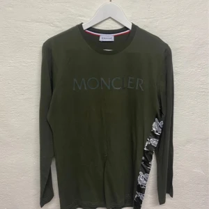 Grön långärmad tröja från Moncler - Snygg mörkgrön långärmad tröja från Moncler med tryckt logga framtill och unikt mönster längs ena sidan. Rund halsringning och diskret tryck på ryggen.  Skick 9/10 Storlek S
