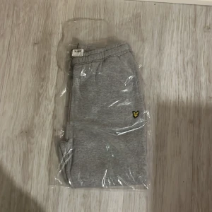 Grå mjukisbyxor från Lyle & Scott Junior - Säljer ett par grå mjukisbyxor från Lyle & Scott Junior med resår i midjan och en liten gul logga på benet. Perfekta för en avslappnad stil och riktigt sköna att ha på sig. Färg: Vintage Grey Heather. 